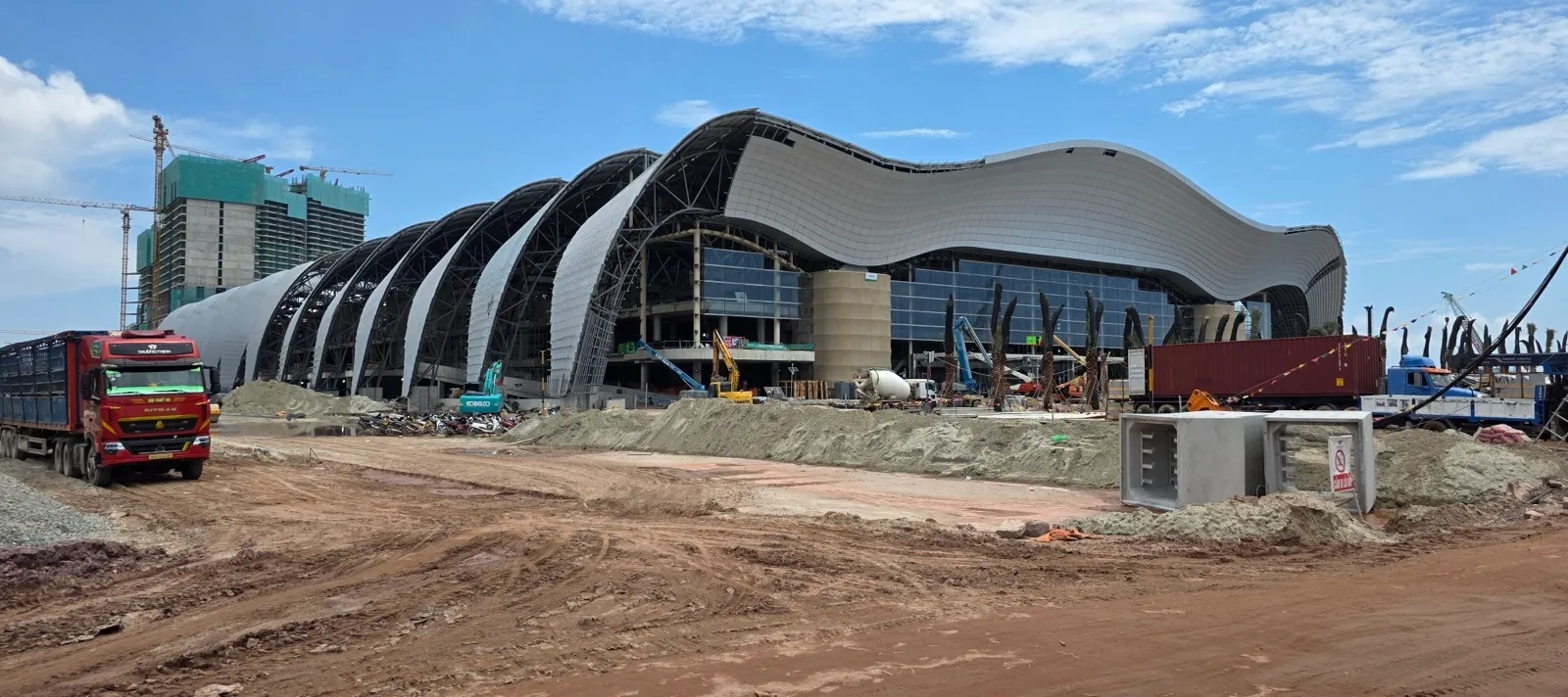 The wave-shaped steel roof of the APEC convention centre on Phu Quoc, still under construction, with a red lorry and heaps of earth in front