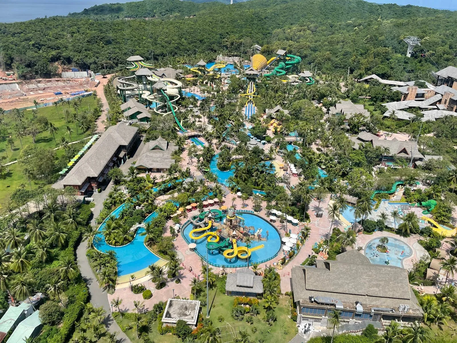 An aerial view of Aquatopia water park: pools, slides and themed buildings among tropical trees
