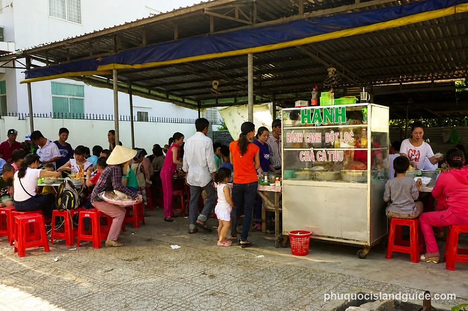 Busy street food stall with diners on red plastic stools