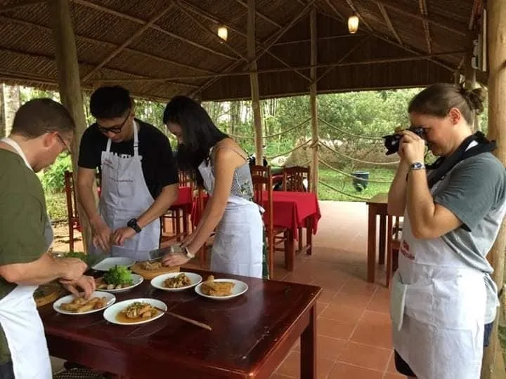 Visitors in aprons cooking at a table under a thatched roof at the pepper farm
