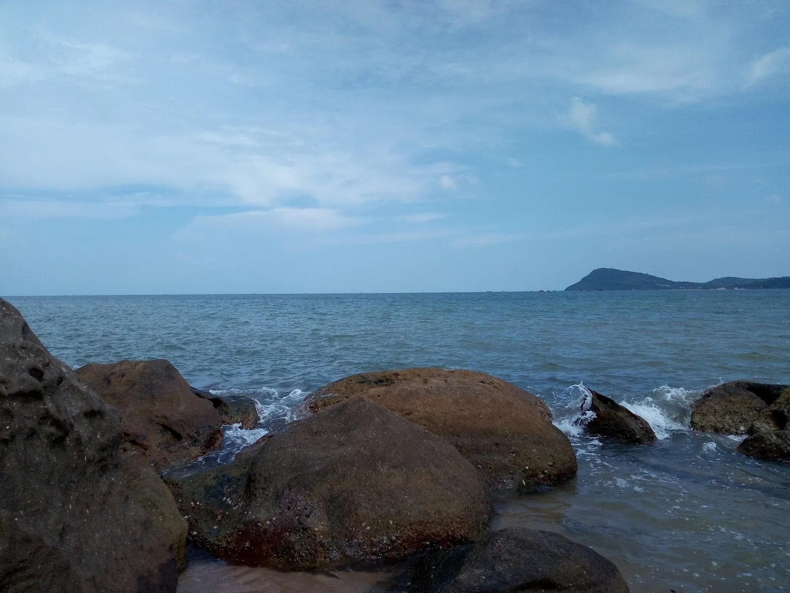 Boulders at the water’s edge at Bai Dam, with a headland across the bay