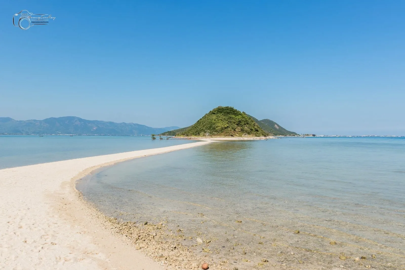 A curving white sandbar running out across clear water to a small green islet at Diep Son