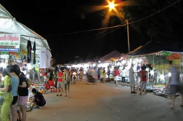 A bustling night market scene with many people browsing various stalls under bright streetlights, creating a lively atmosphere.