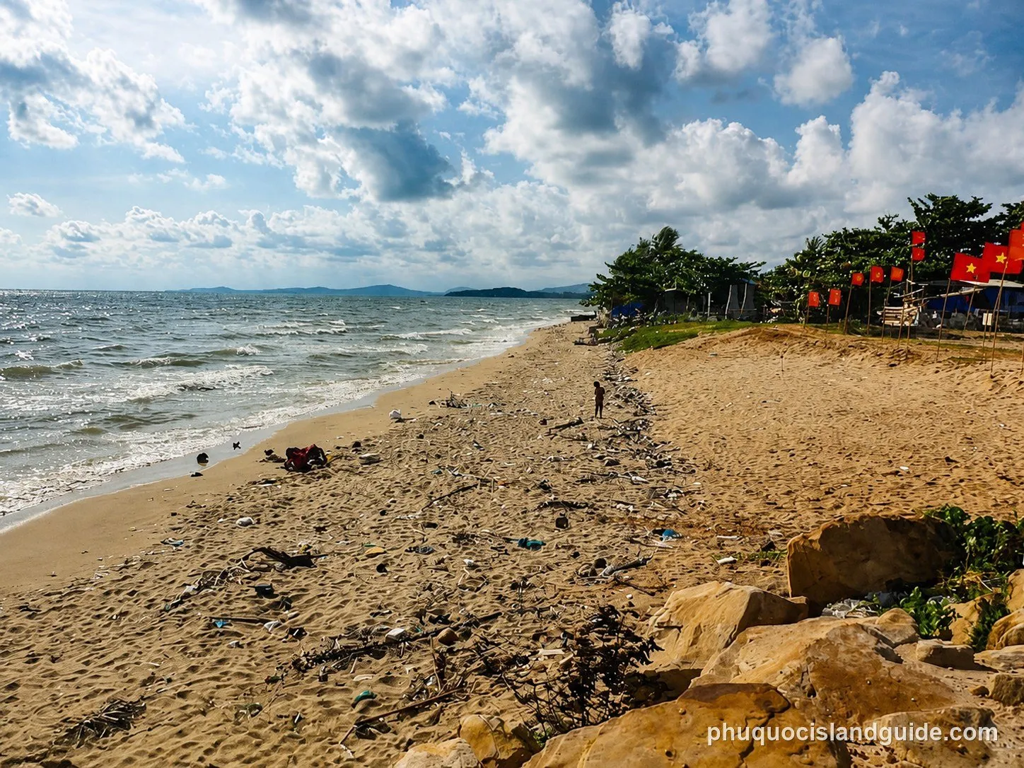 Litter on the sand at Duong Dong beach, with red flags by the shacks