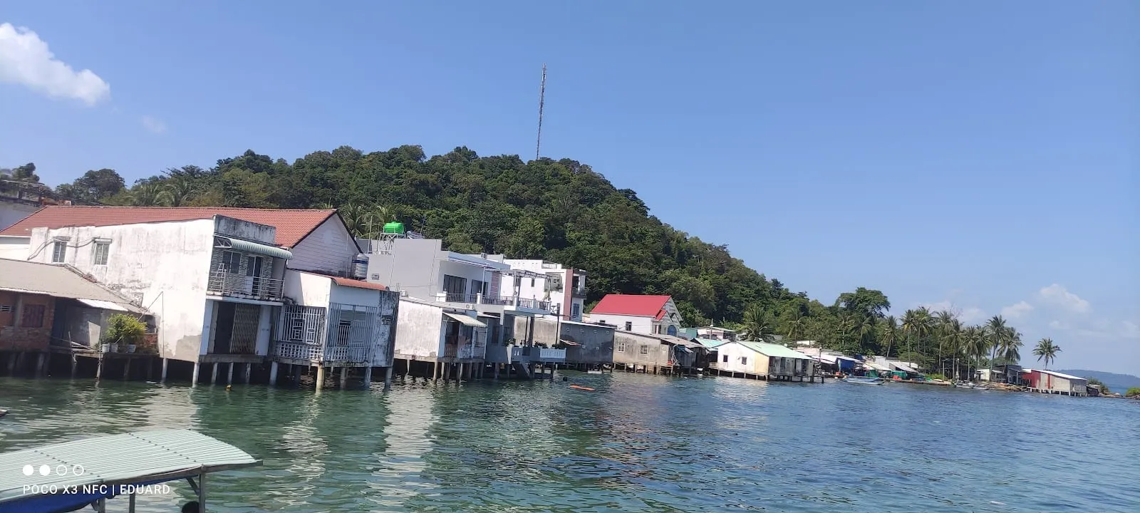 Stilt houses along the shore of a fishing village at Ganh Dau, under a forested hill
