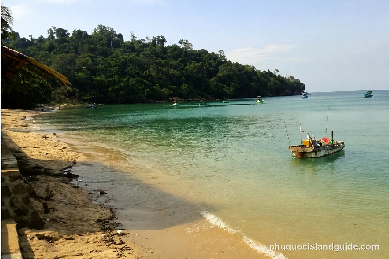 Clear turquoise water and fishing boats below the forested hill at Ganh Dau