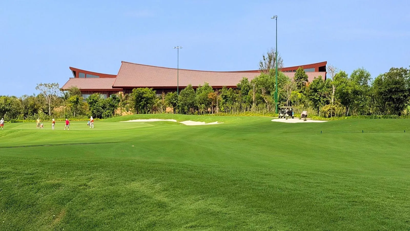 A green fairway with bunkers and the long, low clubhouse roof behind it at Eschuri Vung Bau Golf