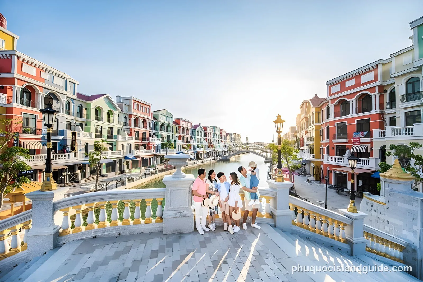 A Venice-style canal lined with brightly coloured shophouses, with a family standing on an ornate stone bridge