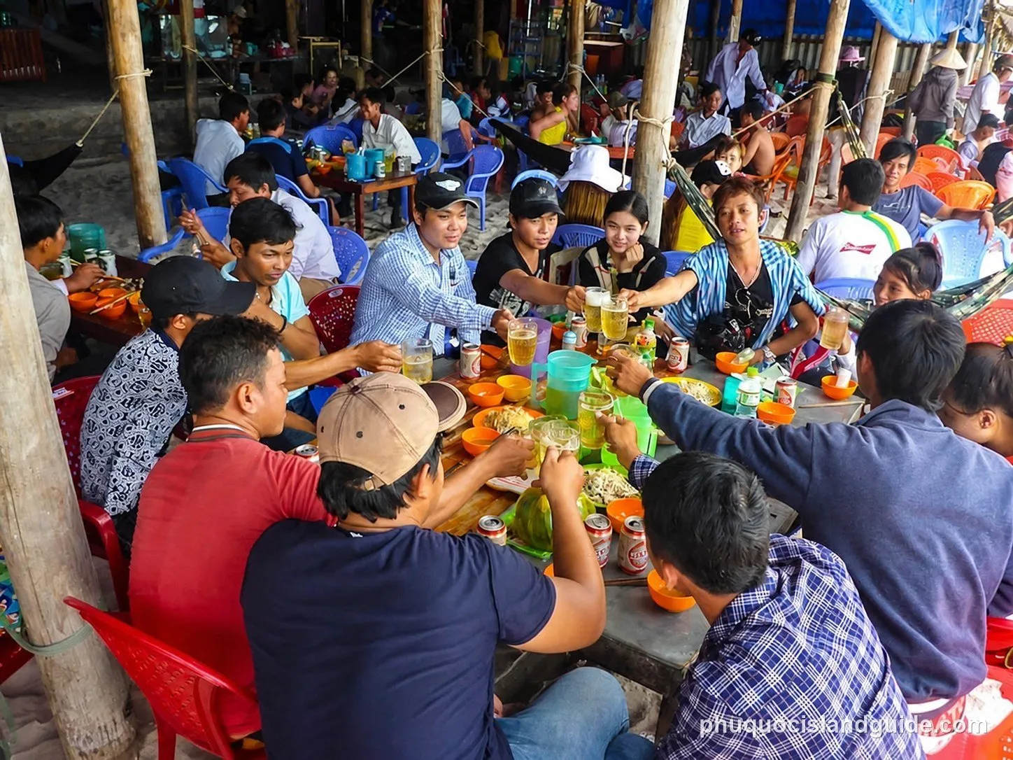 Crowd eating and drinking under a makeshift shelter on the sand at Khem Beach