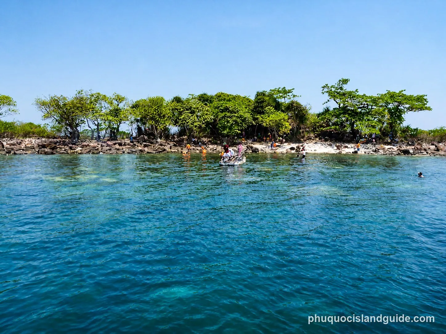 People swimming off a small island with a sandy beach and rocks