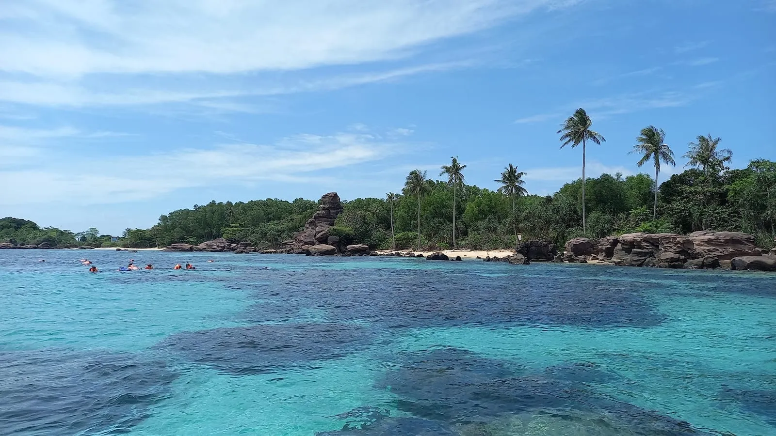 Turquoise water over the shallow reef at Hon Gam Ghi, with palm trees on the island behind