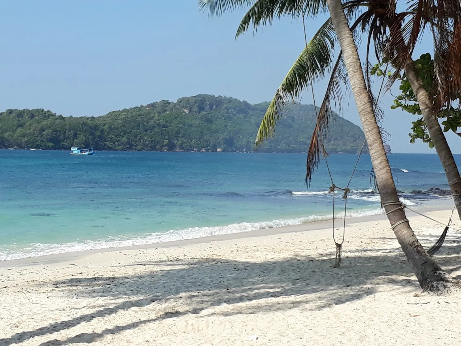A quiet white-sand beach with a palm-tree swing at Hon May Rut, with a green island across the water
