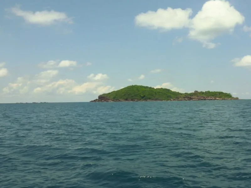 A small tropical island covered in lush green vegetation, surrounded by a calm blue sea under a partly cloudy sky.