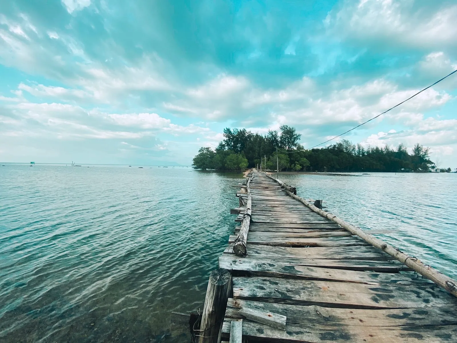 A long wooden walkway across shallow water to the small wooded islet of Hon Mot
