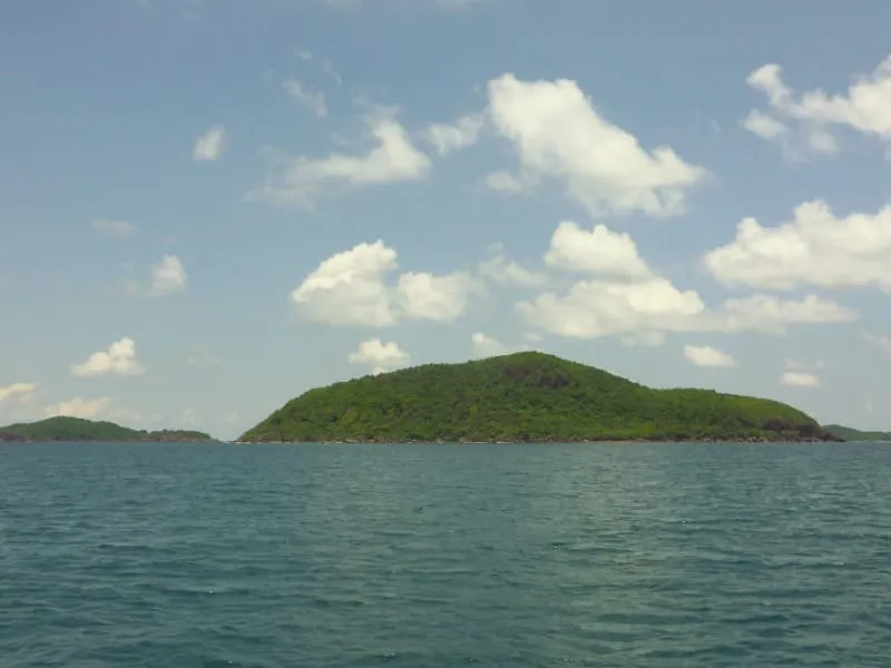 A view of a tropical sea with several green, forested islands under a blue sky with scattered white clouds.
