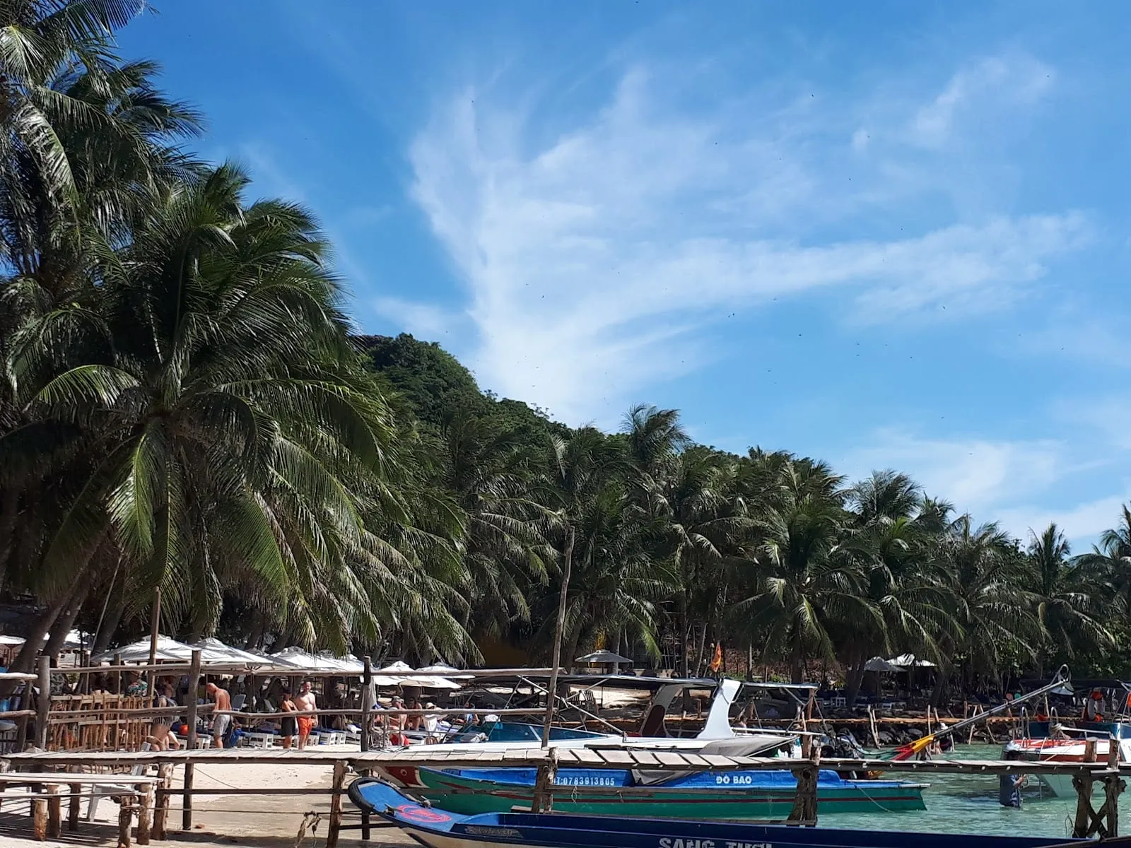 Swimmers in the shallow turquoise water off Hon Vong, with tour boats and an island behind