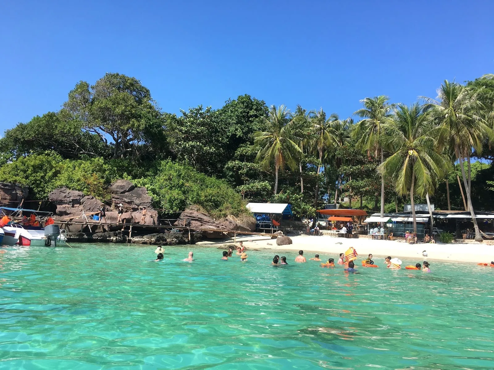 Swimmers in turquoise water off the white-sand beach at Hon Xuong, with palms behind
