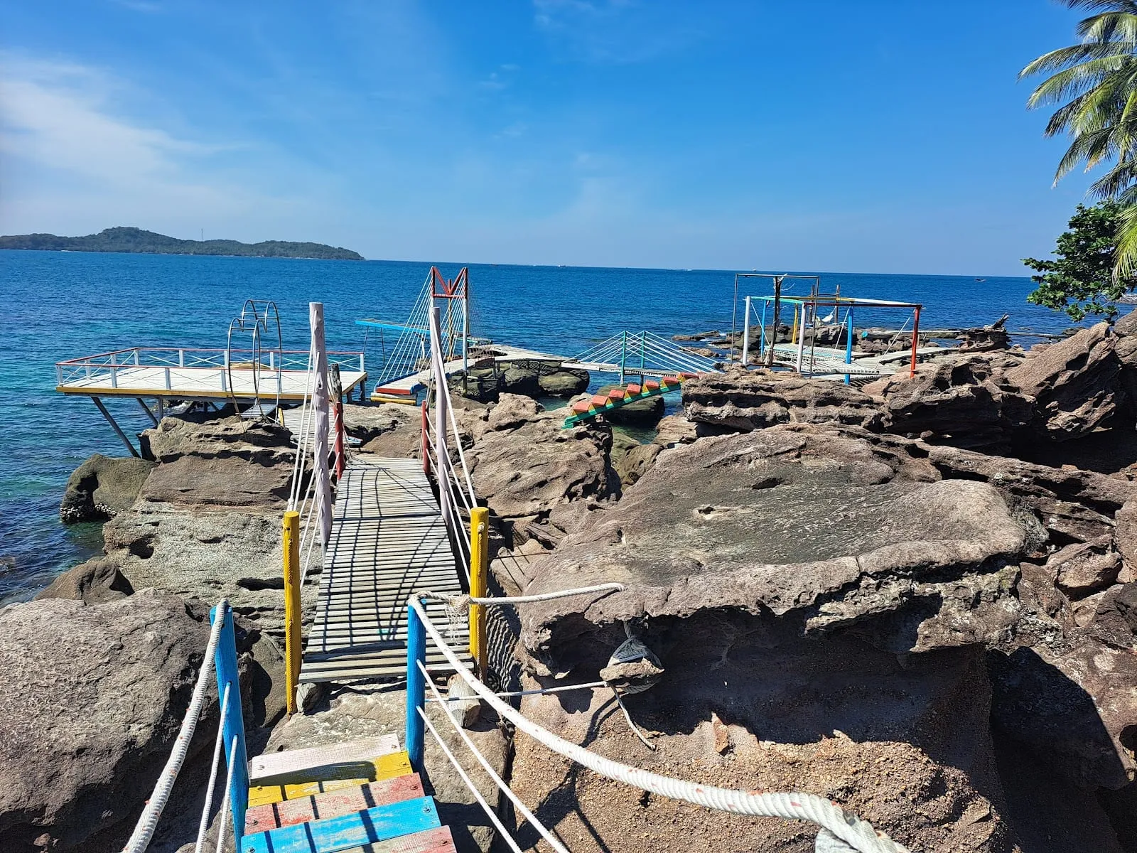 Sandstone rocks and a wooden walkway at Hon Xuong, with the sea and islands behind
