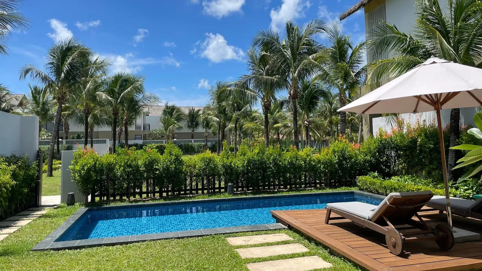 A private pool with sunbeds and a parasol in the garden of a villa among palm trees at New World Phu Quoc Resort