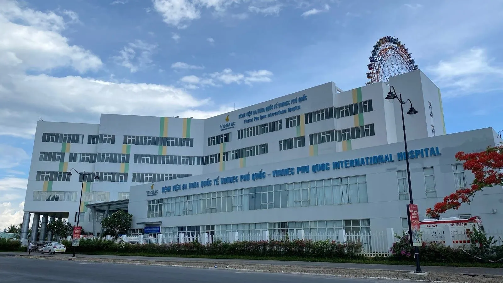 The white building of Vinmec Phu Quoc International Hospital, with the Ferris wheel of Grand World behind it