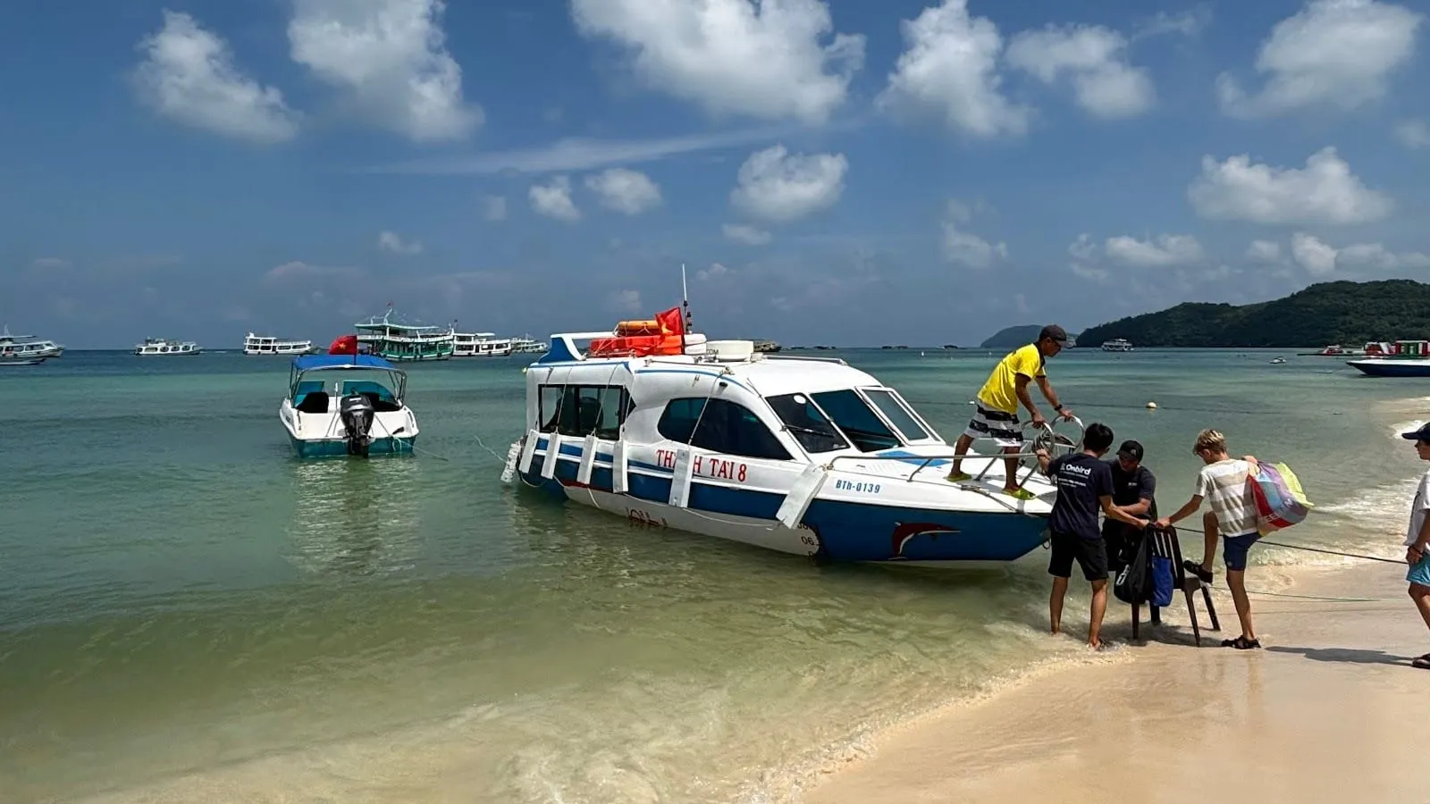 A white speedboat pulled up on a sandy beach in the An Thoi islands, with snorkellers carrying their gear ashore