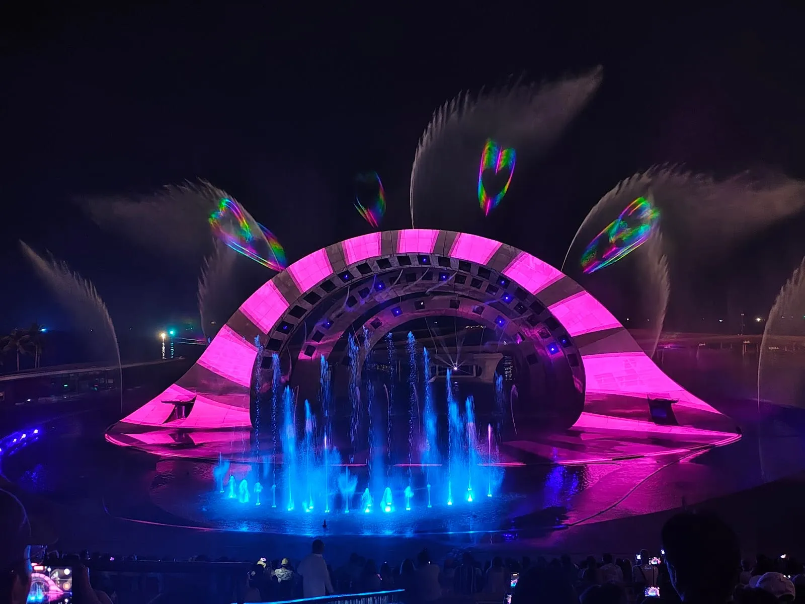 The Kiss of the Sea stage lit in pink and purple during the show, with fountains in front