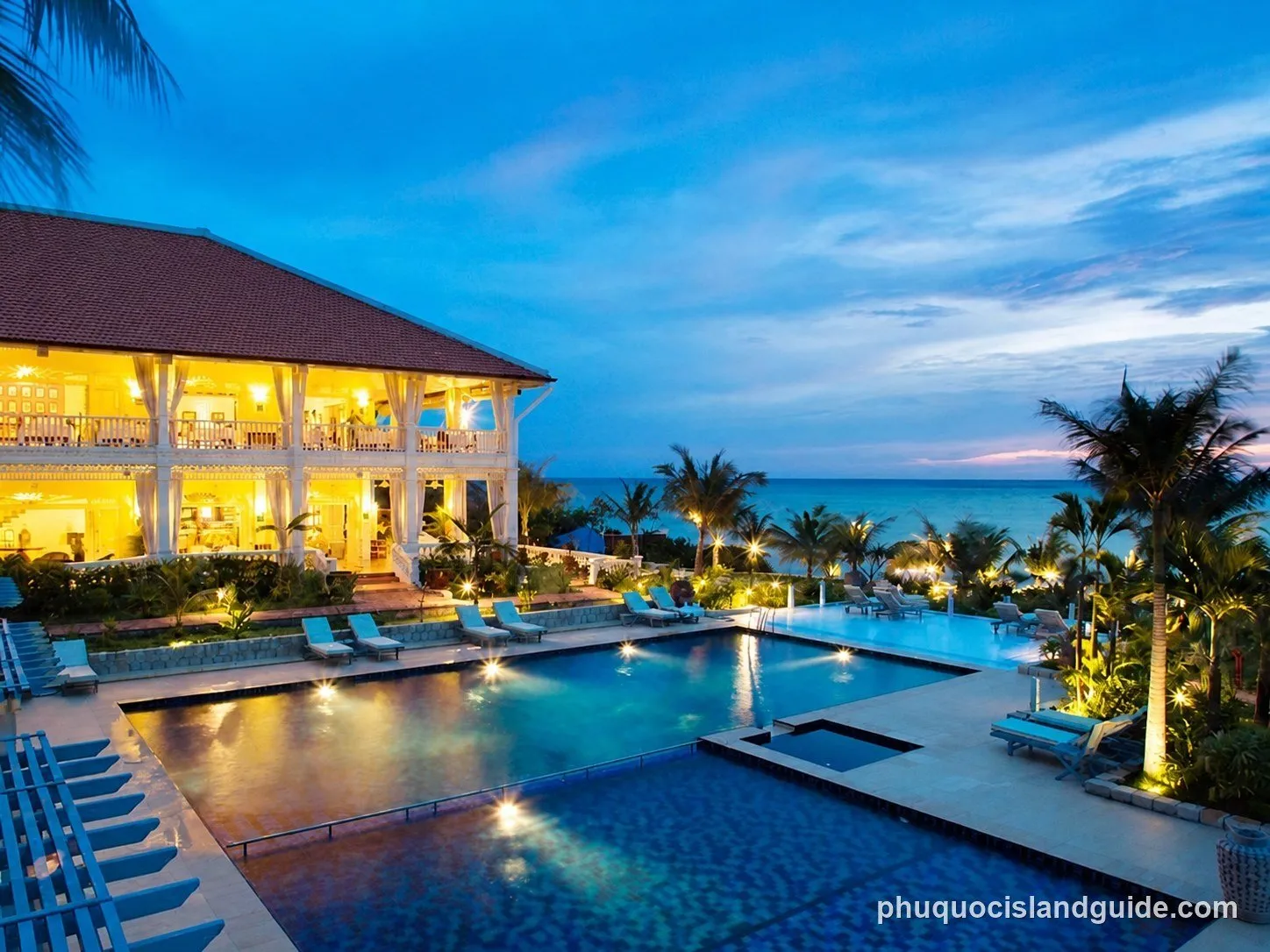 Resort pool and palm trees by the sea at dusk