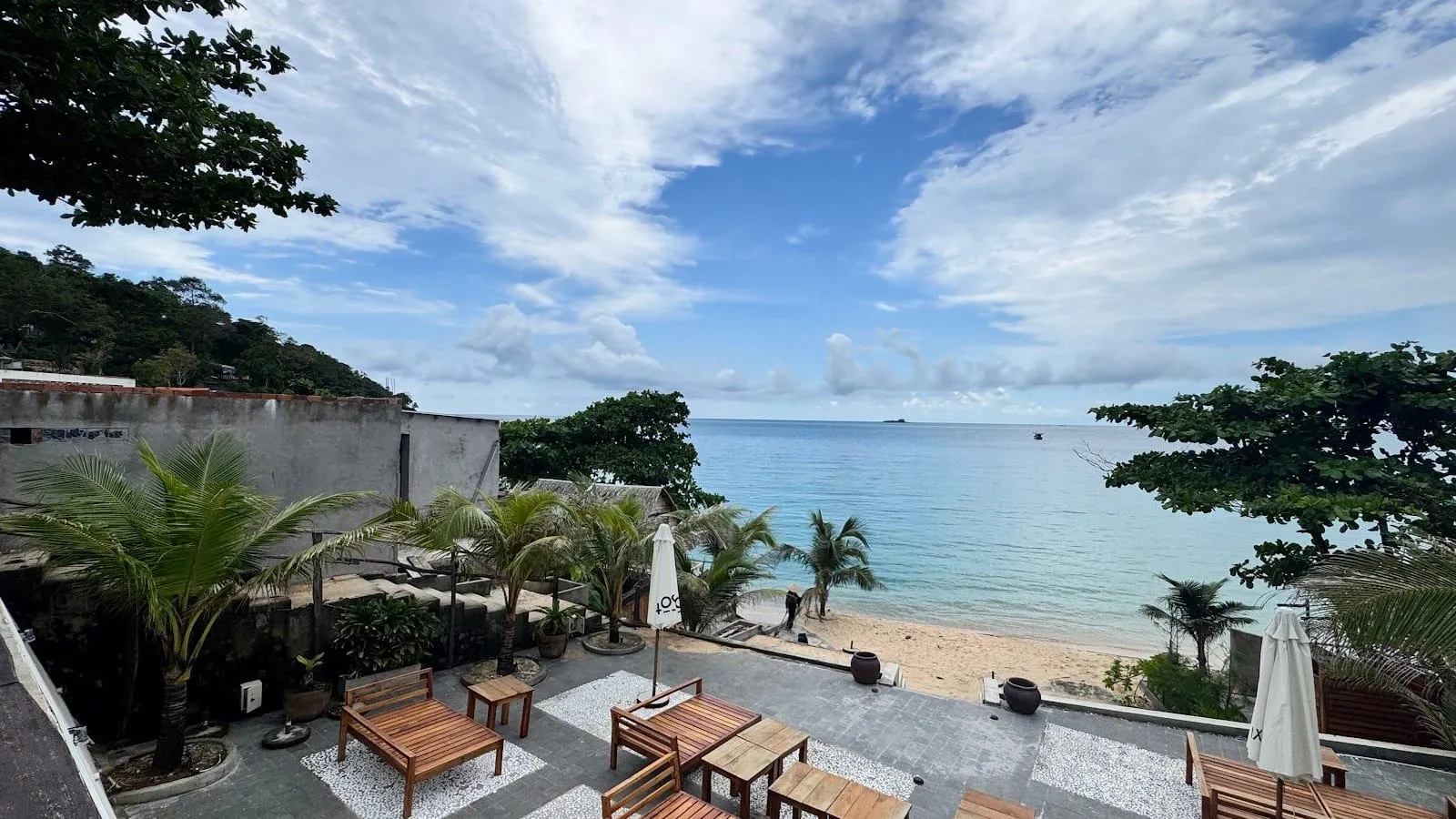 A quiet beach with palm trees and a terrace of sunbeds under a partly cloudy sky on the north-west coast of Phu Quoc in November