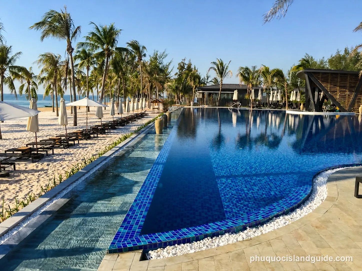 Large pool next to a white sand beach with sunbeds and parasols