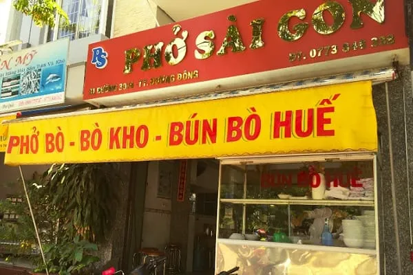 A vibrant storefront of a Vietnamese restaurant named ‘Phở Sài Gòn’ with yellow and red signs advertising ‘Phở Bò - Bò Kho - Bún Bò Huế’.