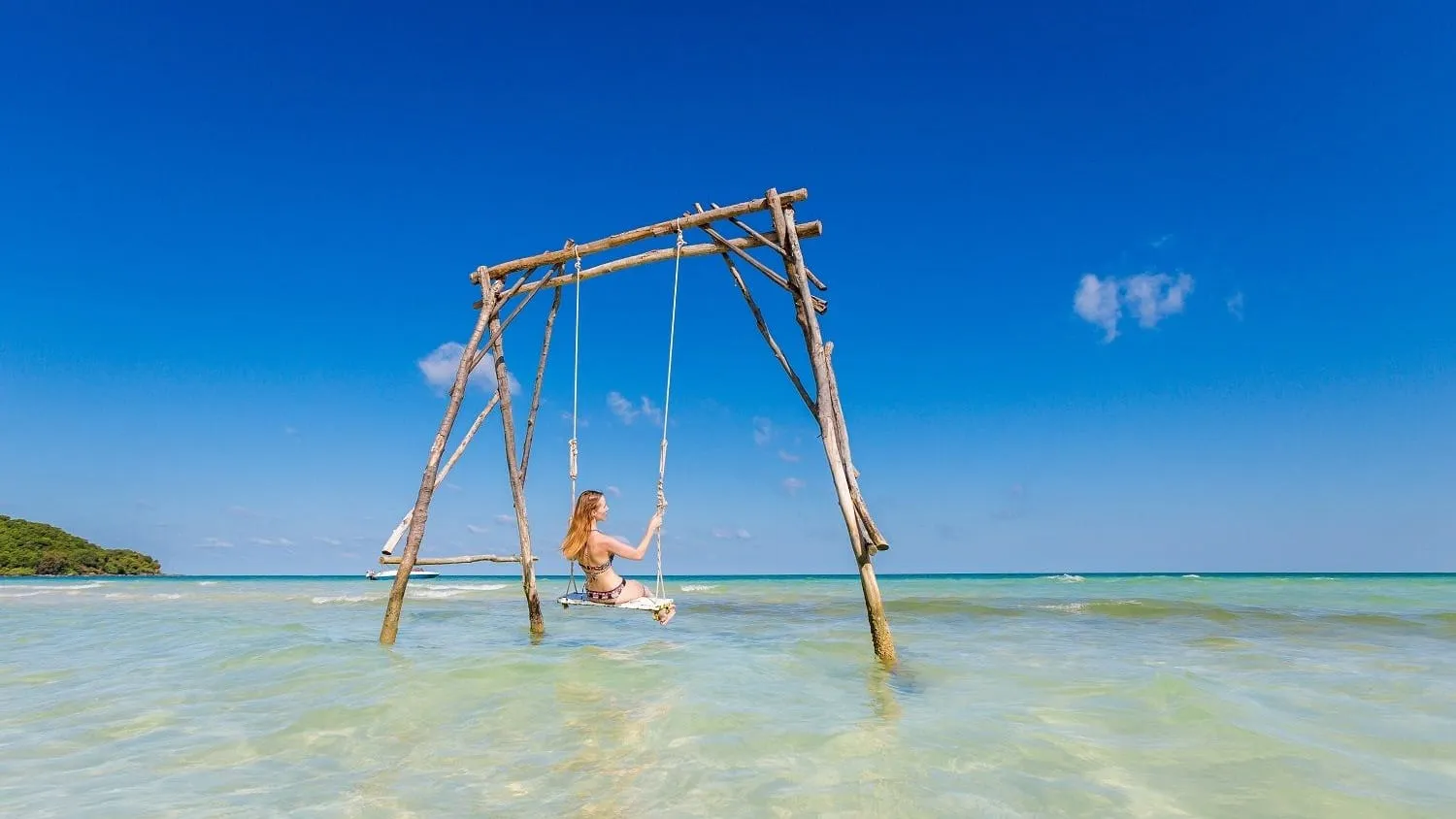 A wooden swing standing in shallow turquoise water at Sao Beach under a bright blue sky