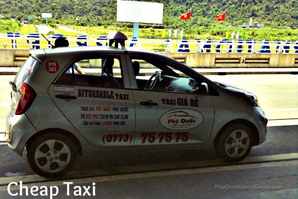 A silver taxi car with ‘Affordable Taxi’ and ‘Phu Quoc’ branding on its side, parked on a road. Green hills and Vietnamese flags are visible in the background.