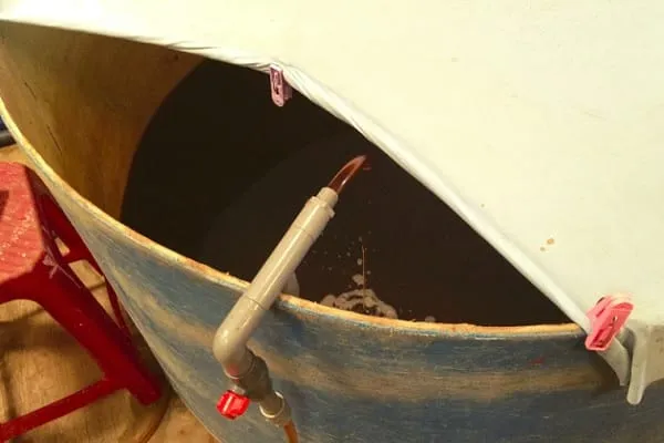 Dark fish sauce draining from an open vat through a tap