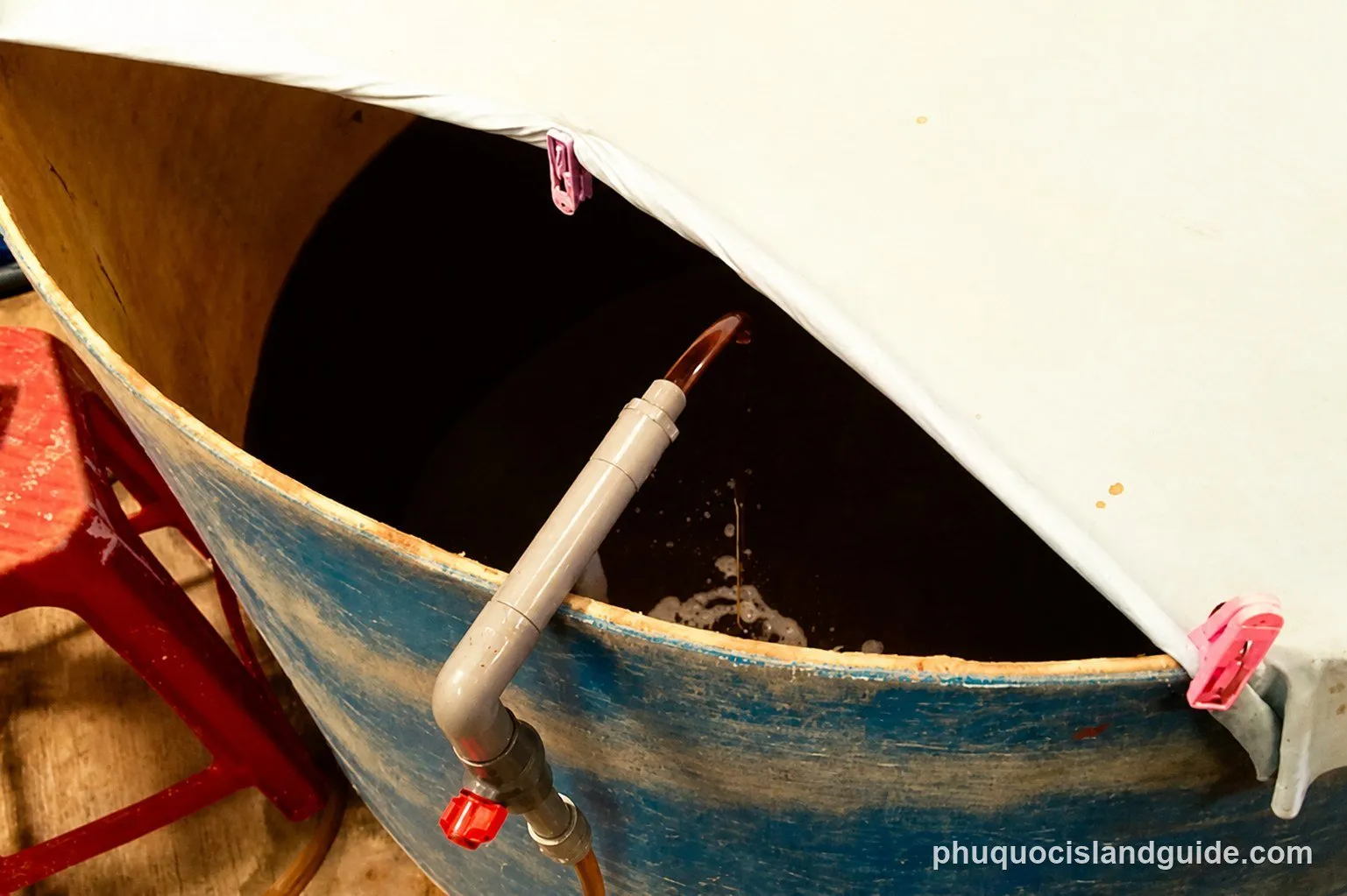 Dark fish sauce draining from an open vat through a tap