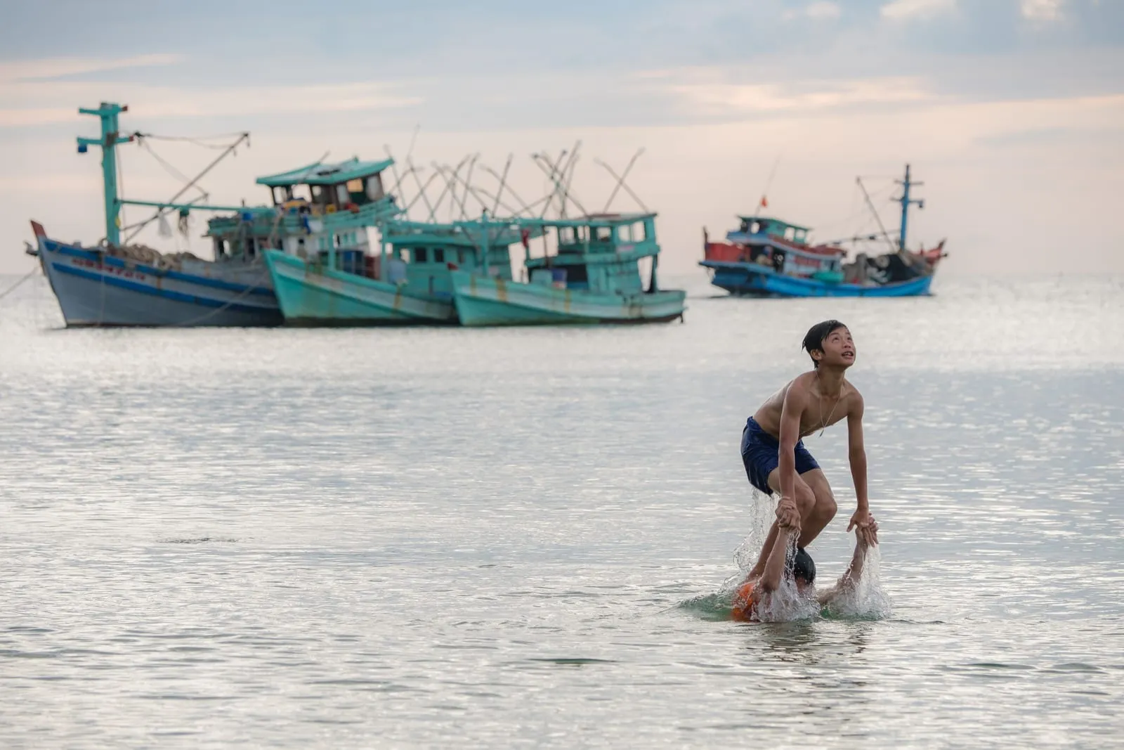 A fisherman wading in shallow water near moored fishing boats off Phu Quoc