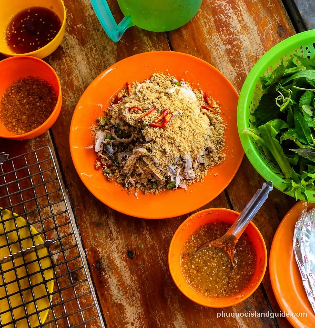 Overhead view of a Vietnamese seafood salad (gỏi) on an orange plate, topped with crushed peanuts and chili, served with fresh herbs and dipping sauces on a wooden table.