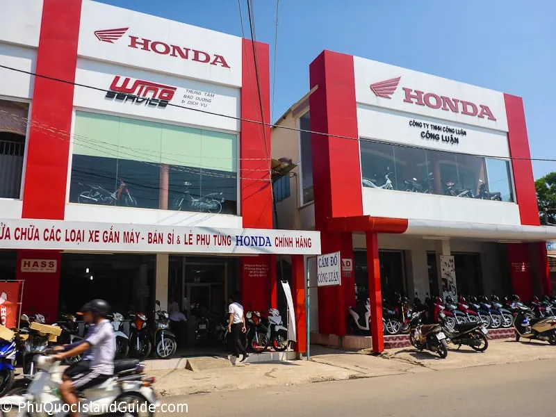 A street view of two red and white Honda motorcycle dealerships and service centers in Vietnam, with many motorbikes parked outside.