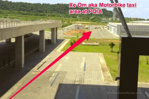 An outdoor area with an elevated road, a parking lot, and buildings, with a red arrow pointing to the motorbike taxi waiting area at Phu Quoc airport.