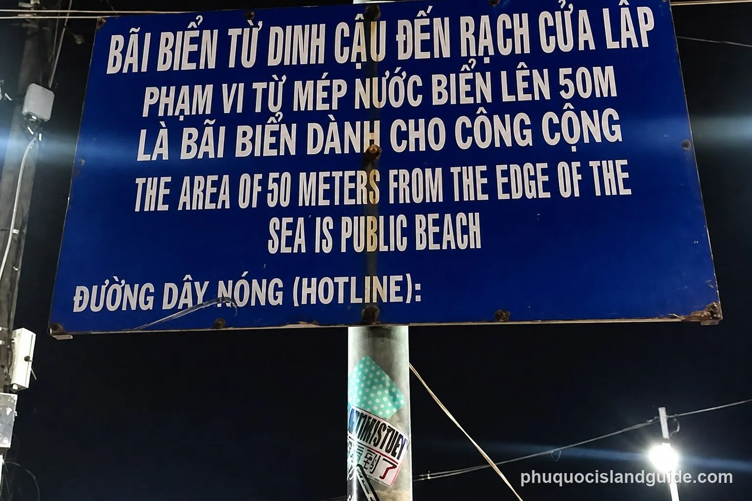 A blue and white sign on Phu Quoc marking a stretch of beach as public, with a hotline number