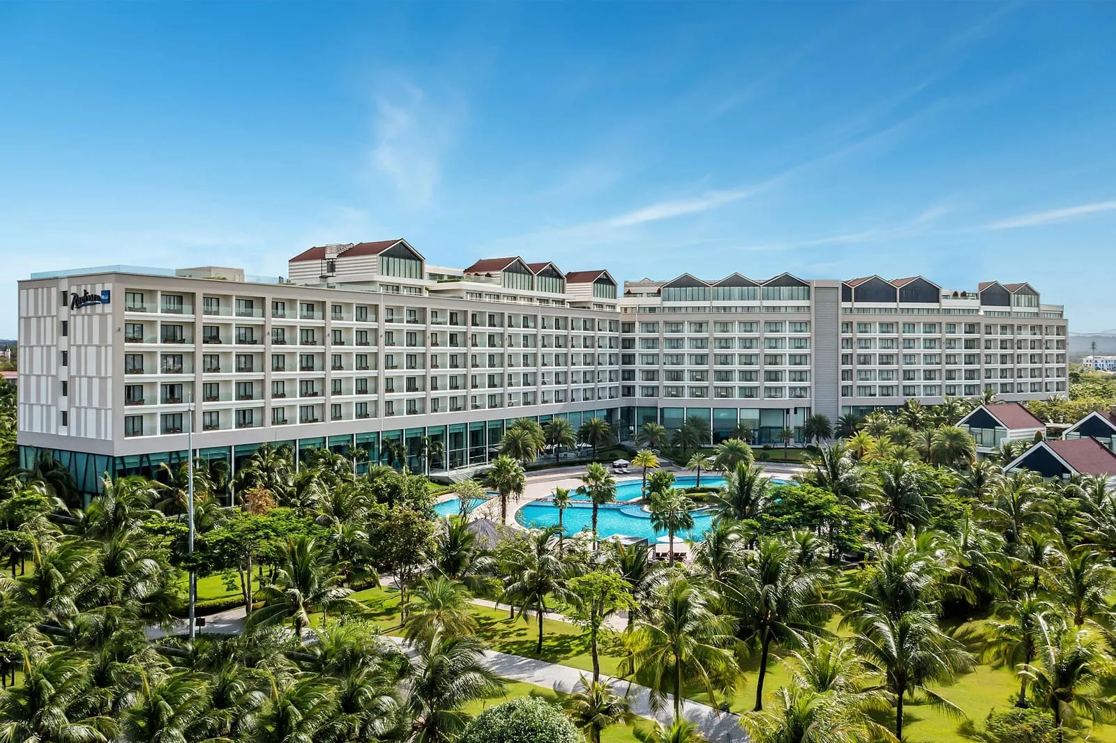 The Radisson Blu Resort building with its logo on the facade, a lagoon-shaped pool and dense palm gardens in front