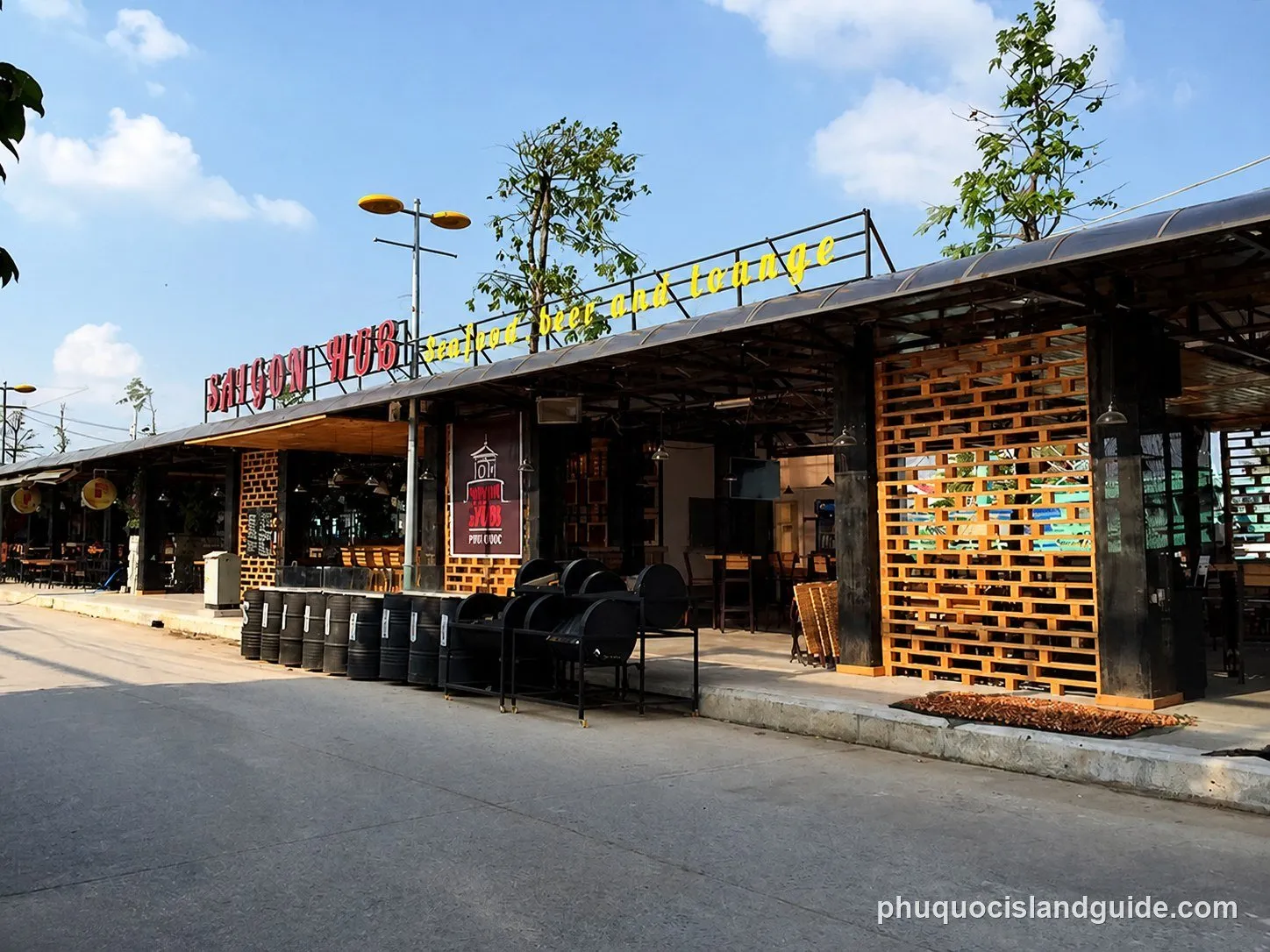 Street view of Saigon Hub, an open-fronted bar and lounge with a yellow and red sign, timber pallet screens and outdoor seating