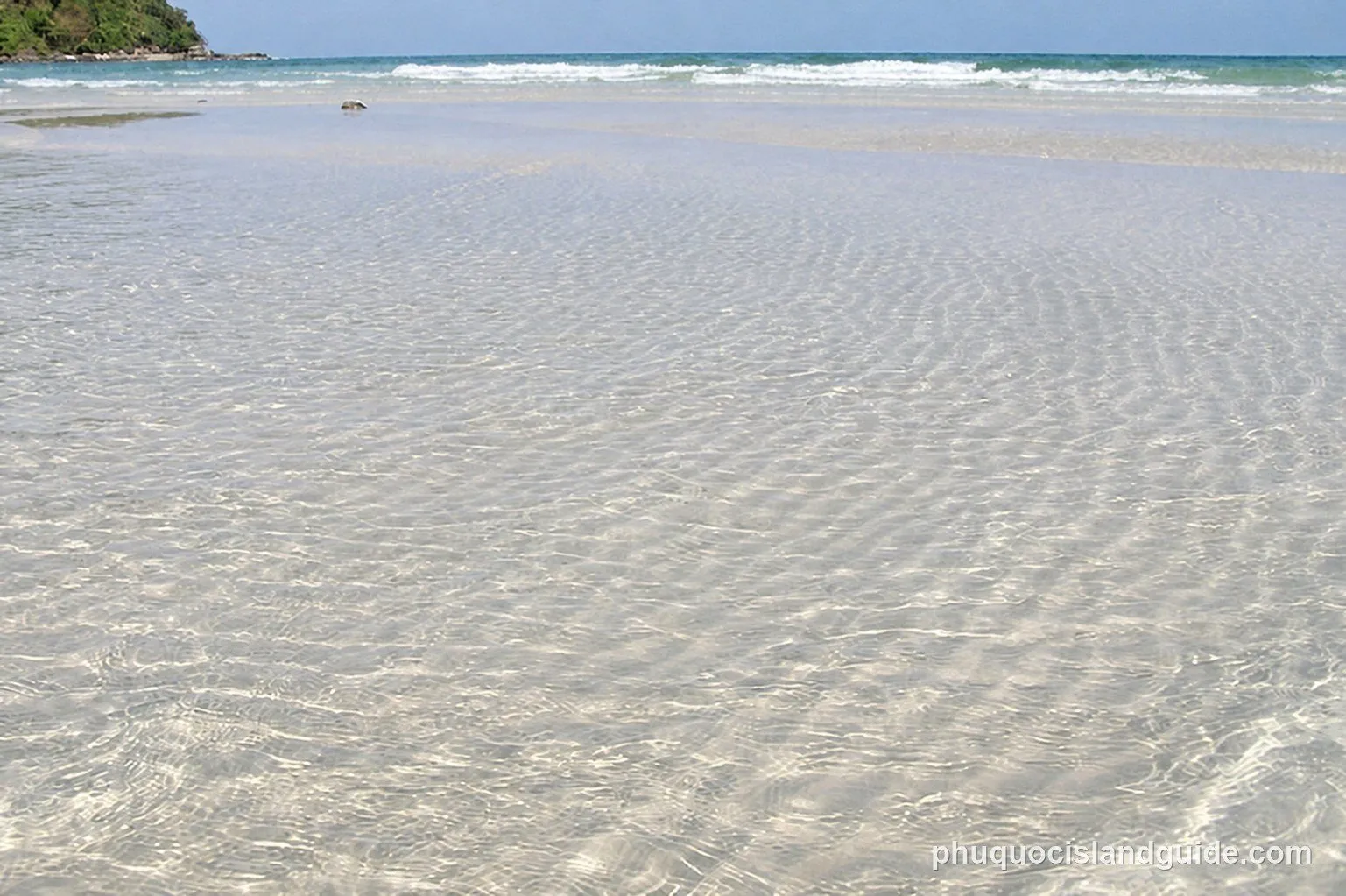Clear shallow water over the sand at Sao Beach, with a green headland