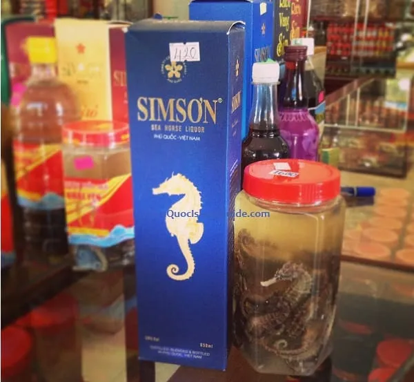 A blue box of Simson Sea Horse Liquor next to a clear jar containing preserved seahorses, with other bottles blurred in the background.