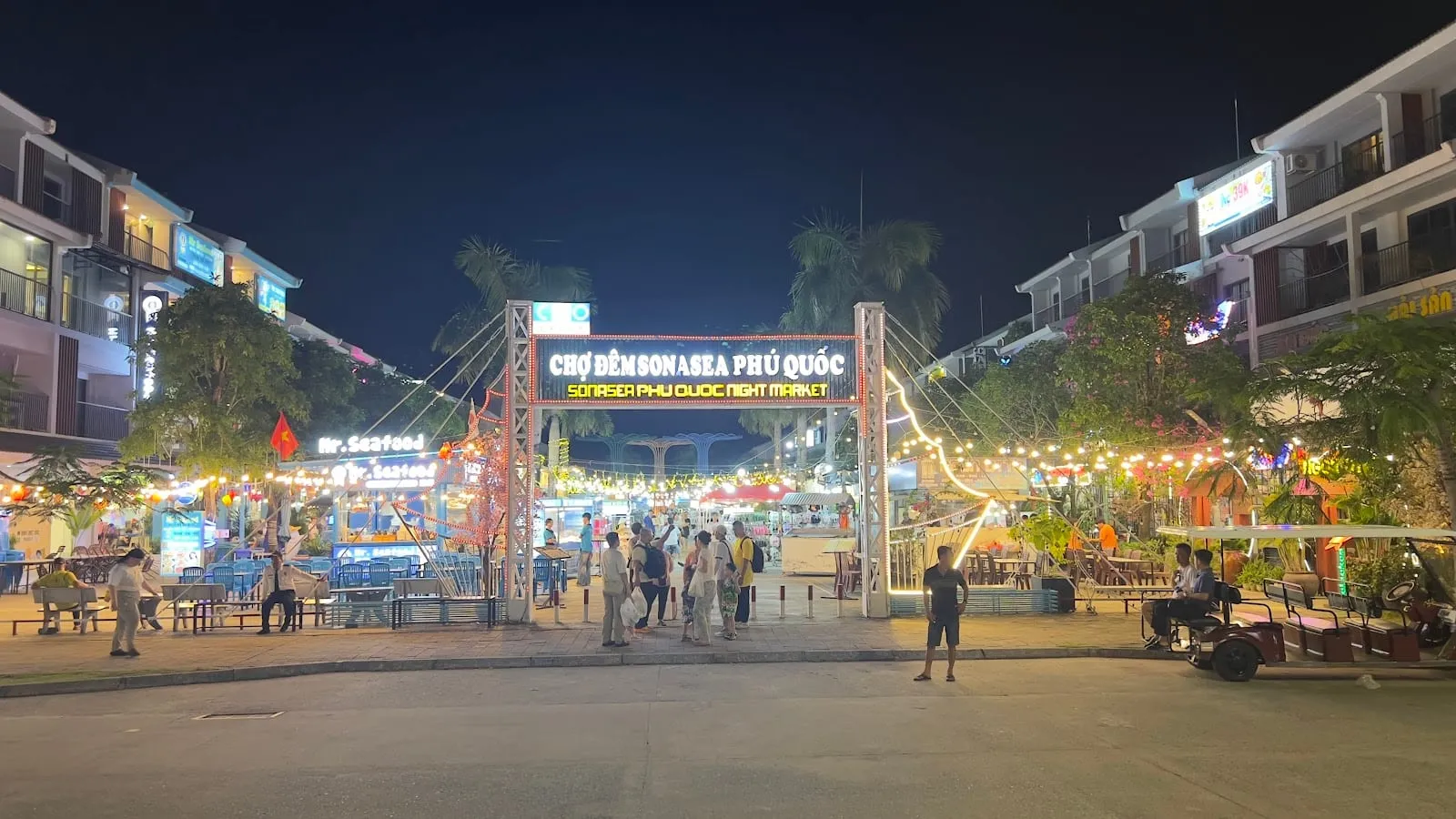The lit gate of the Sonasea night market at Long Beach, with stalls and shoppers in the evening