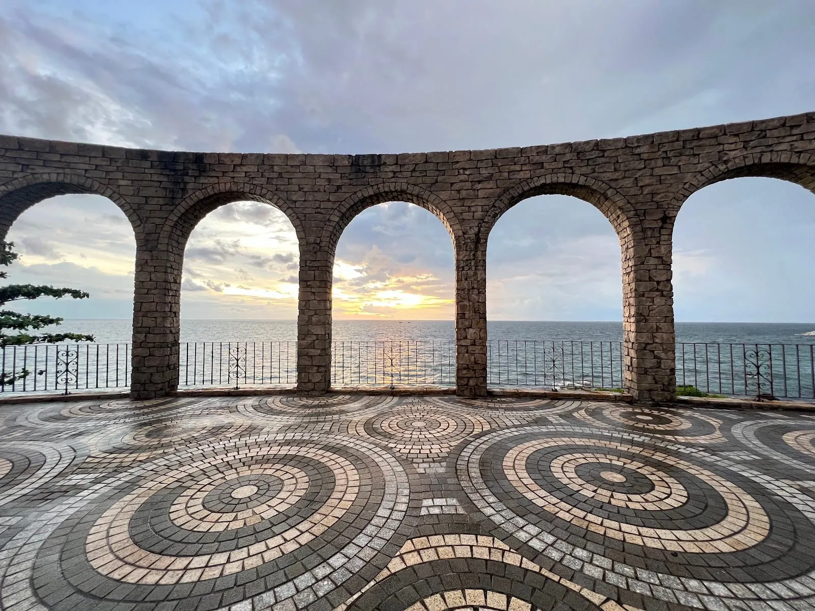 A terrace of stone arches overlooking the sea at sunset in Sunset Town