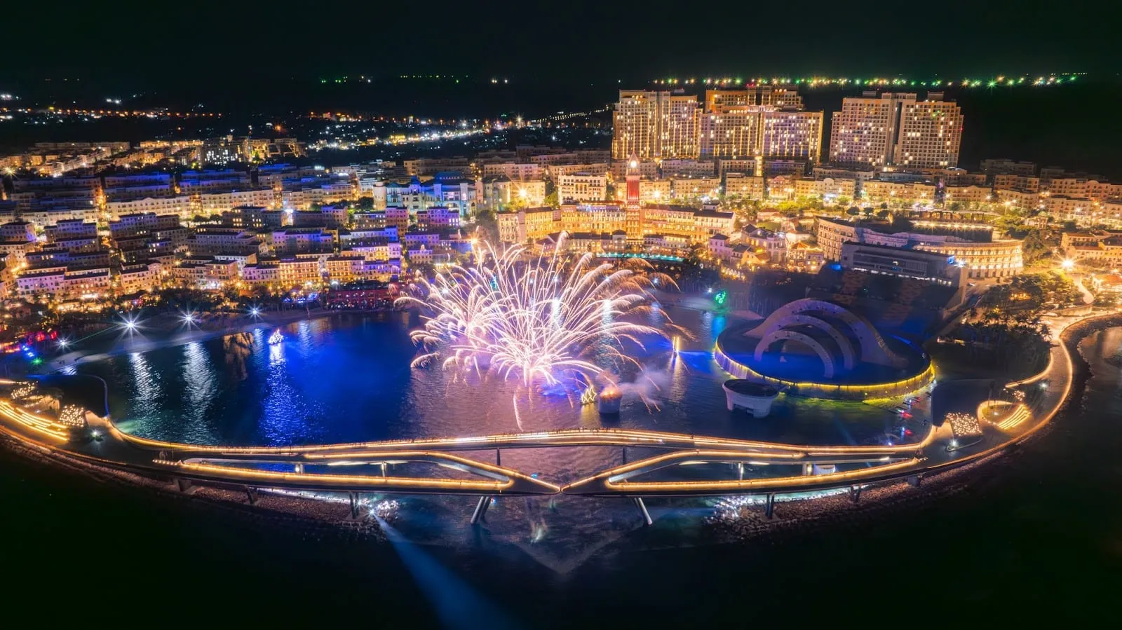 Fireworks over the Kiss of the Sea stage and the lights of Sunset Town at night, seen from above