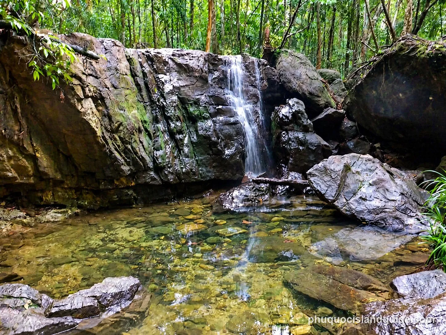 Small waterfall over dark rocks into a clear pool at Suoi Tranh