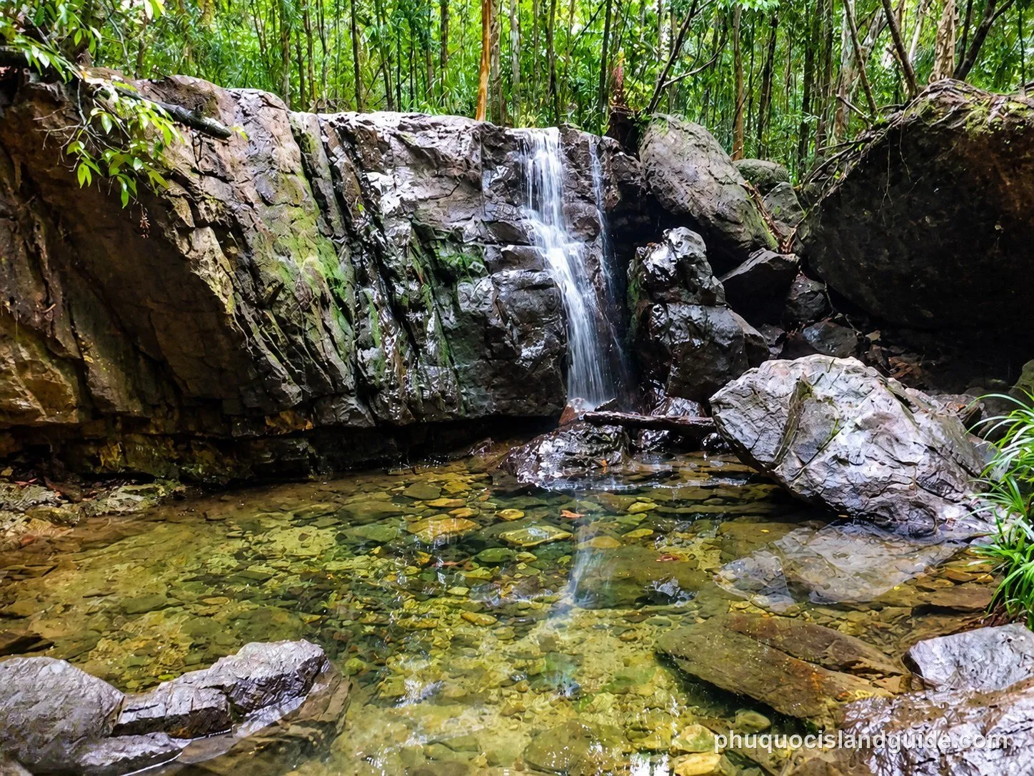 Small waterfall over dark rocks into a clear pool at Suoi Tranh